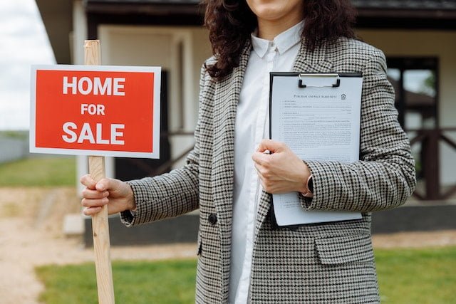 Real estate agent putting a for sale sign in front of a property