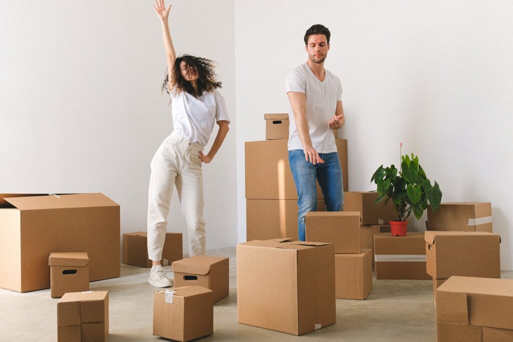 A young couple dancing in front of a pile of cardboard boxes